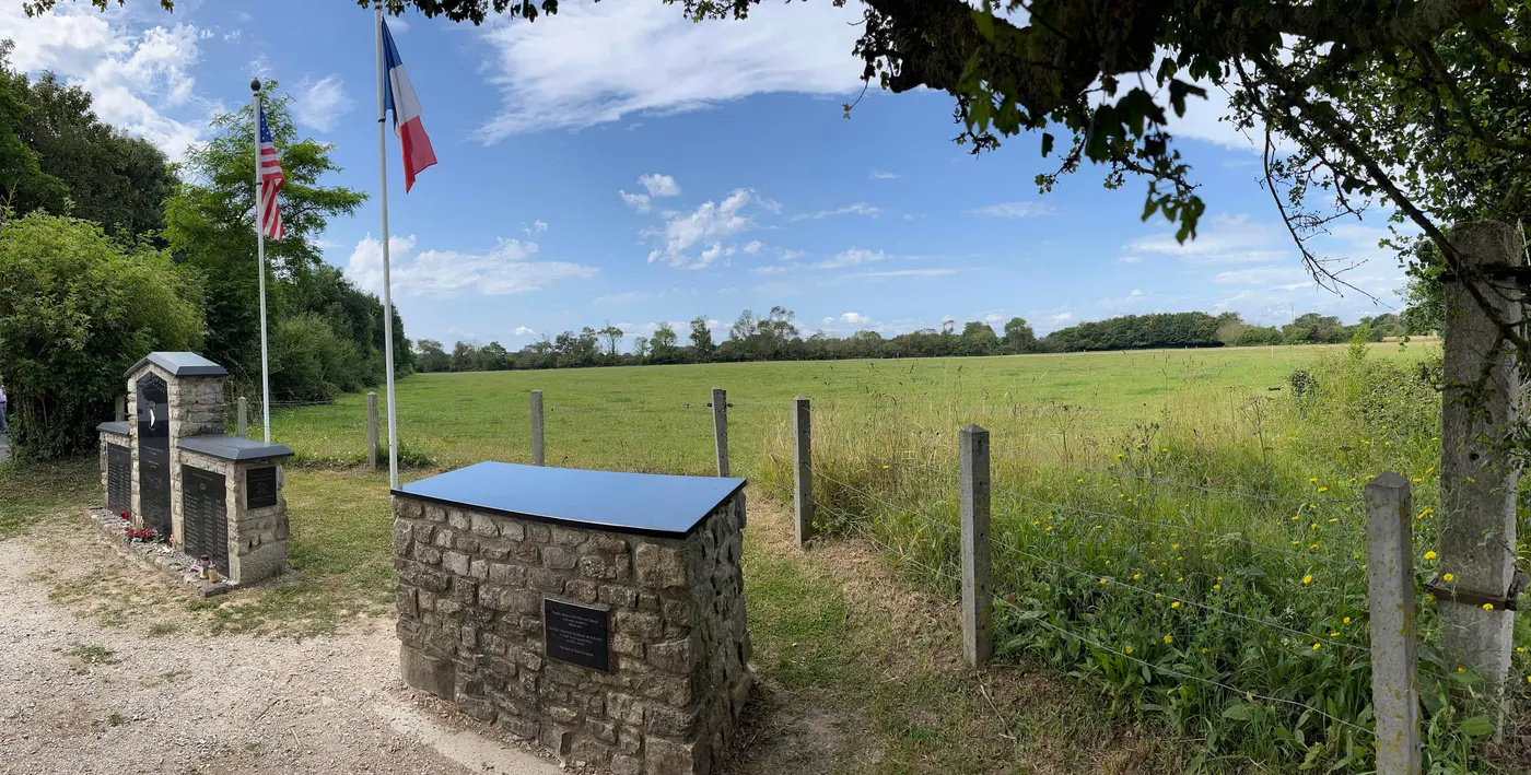 A flat green Normandy field behind a wire fence, bounded by a distant treeline.