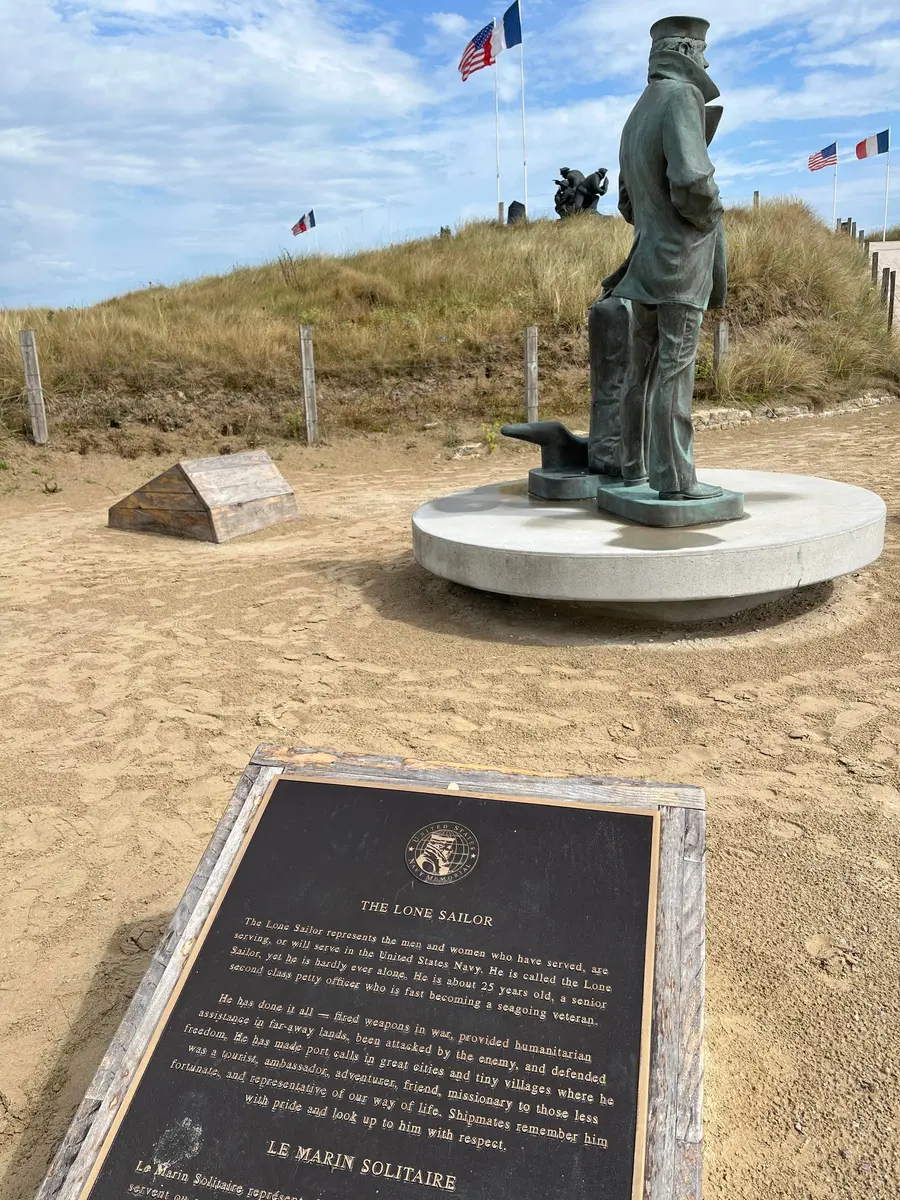 A tall stone memorial to the United States Navy standing on the dunes at Utah Beach.