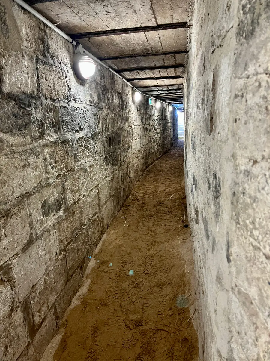A narrow covered concrete trench running between two German bunkers, lit from the far end.